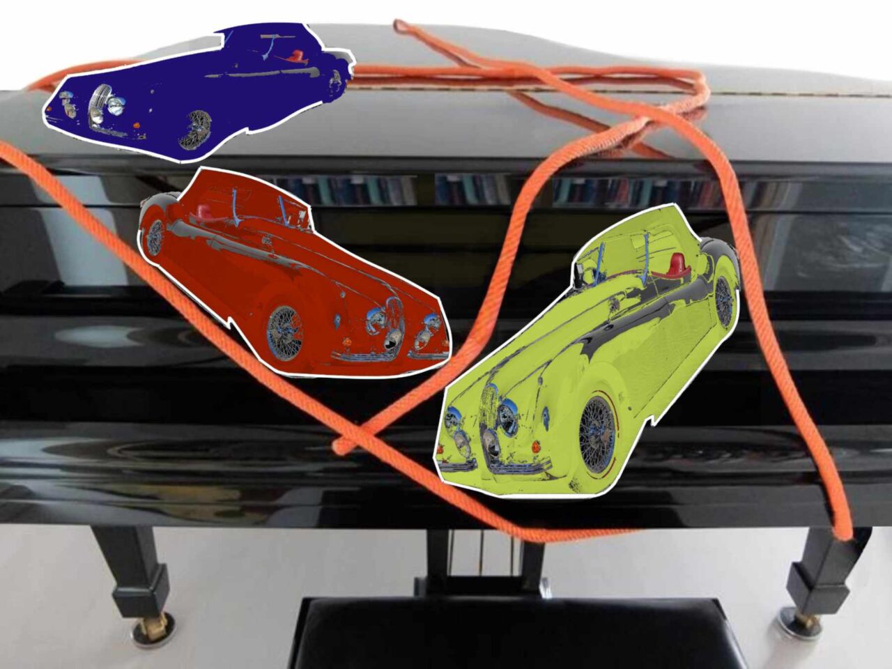 Drei Oldtimer fahren symbolisch über das geschlossene Flügelklavier. Den geschlossenen Klavierflügel.